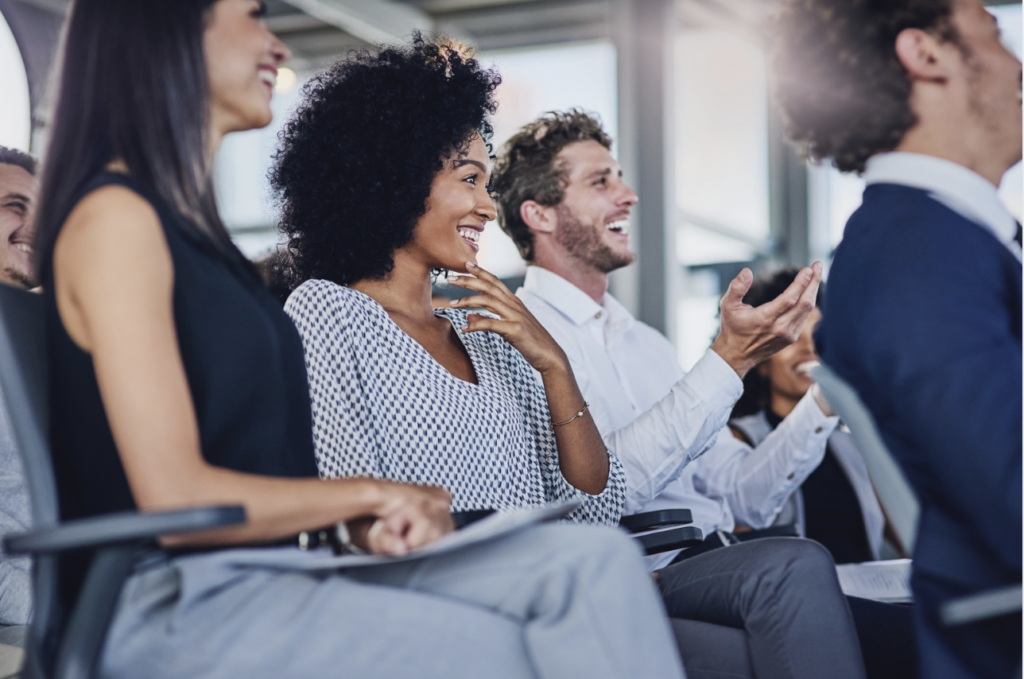 Diverse group of corporate employees listening to a presentation and smiling.