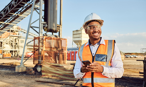 smiling man in a high-visibility vest in from of heavy equipment