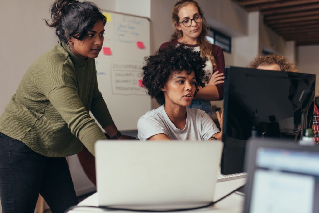 Three office workers looking at a desktop together.