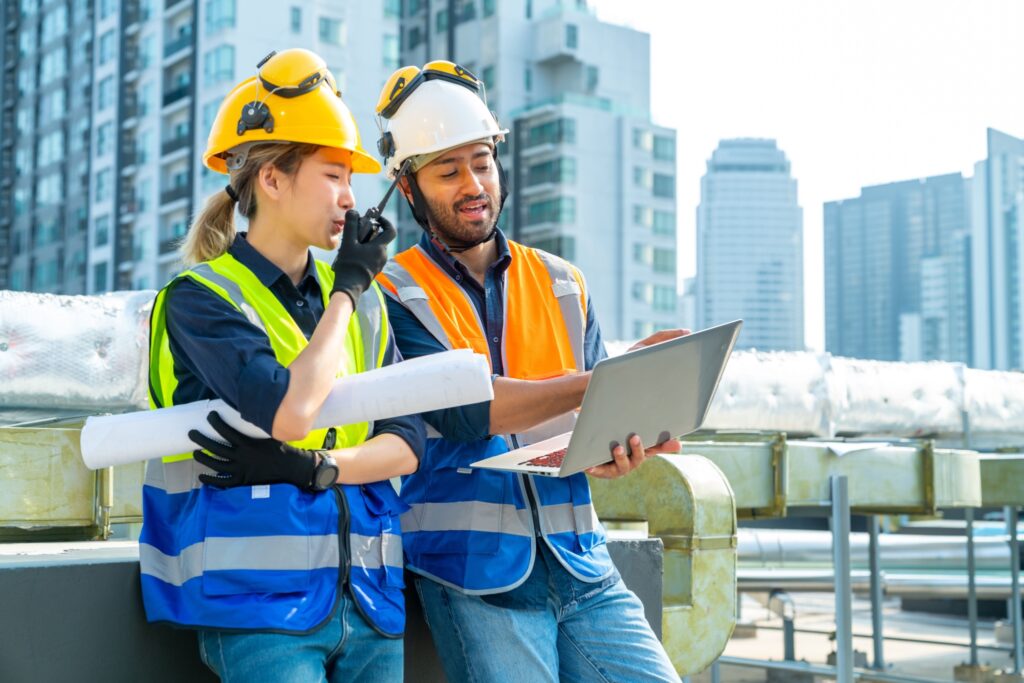 Two young construction workers on site, consulting a laptop.