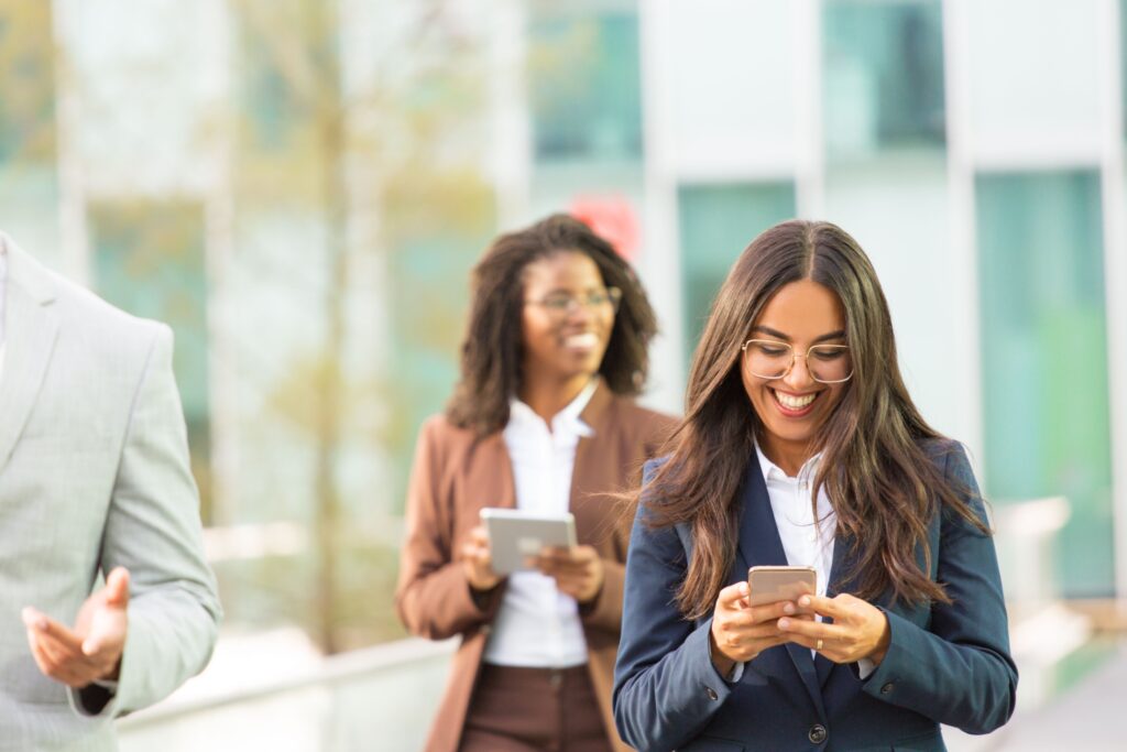Two young corporate colleagues consulting mobile devices as they walk through an open office.