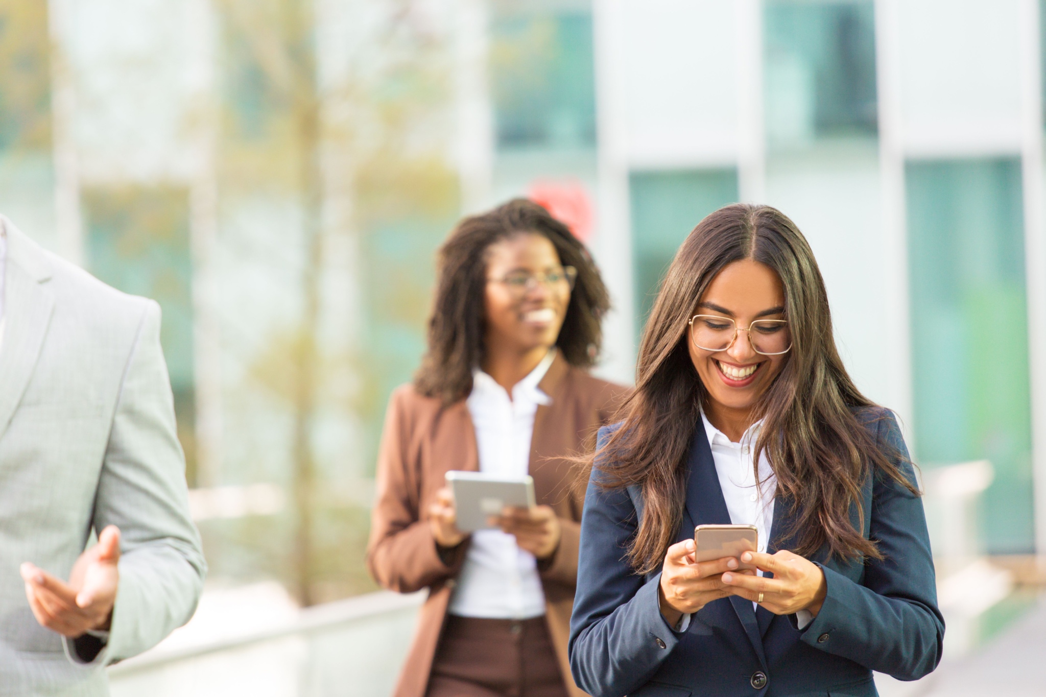 Two young corporate colleagues consulting mobile devices as they walk through an open office.